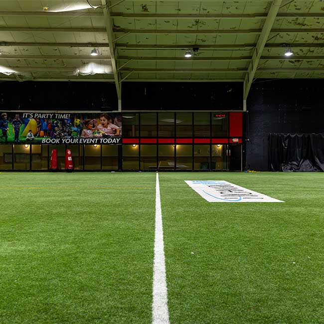 Indoor Fitness Turf Field Rental with white center line and party event banner on the wall.