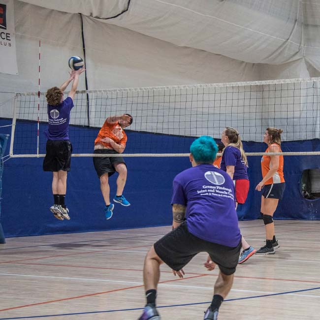 Four people playing Friday Night Pickup Volleyball on an indoor court.